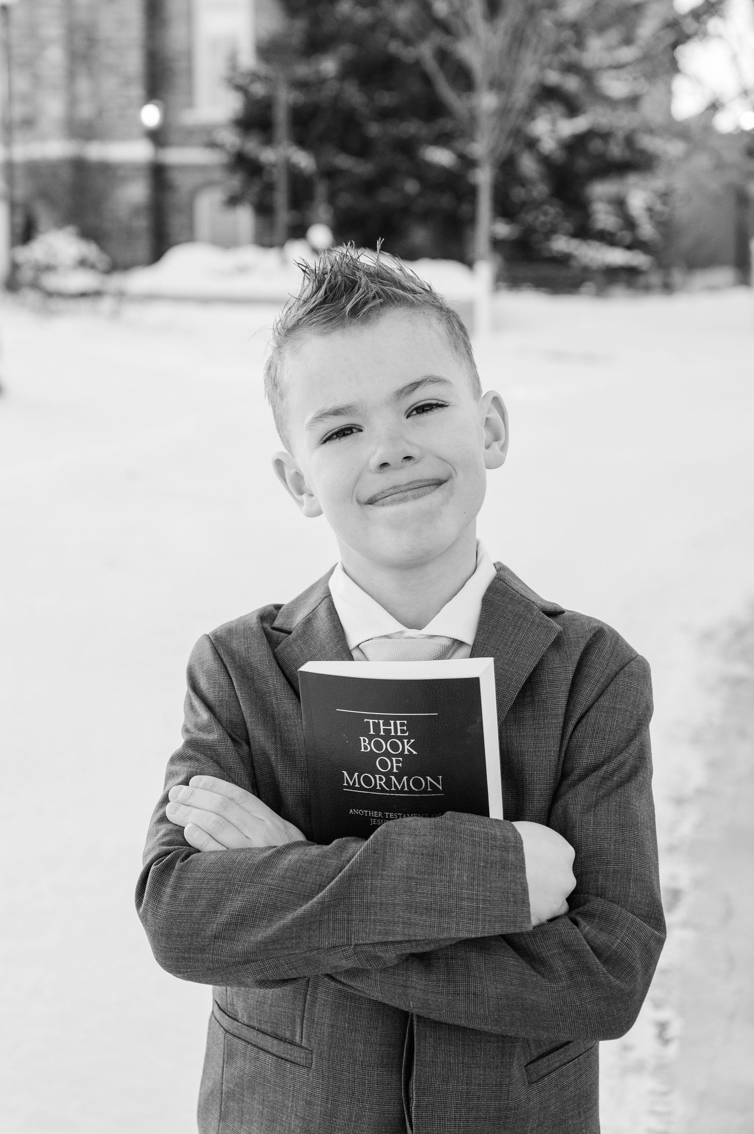 A black and white portrait of someone holding The Book of Mormon against their chest.