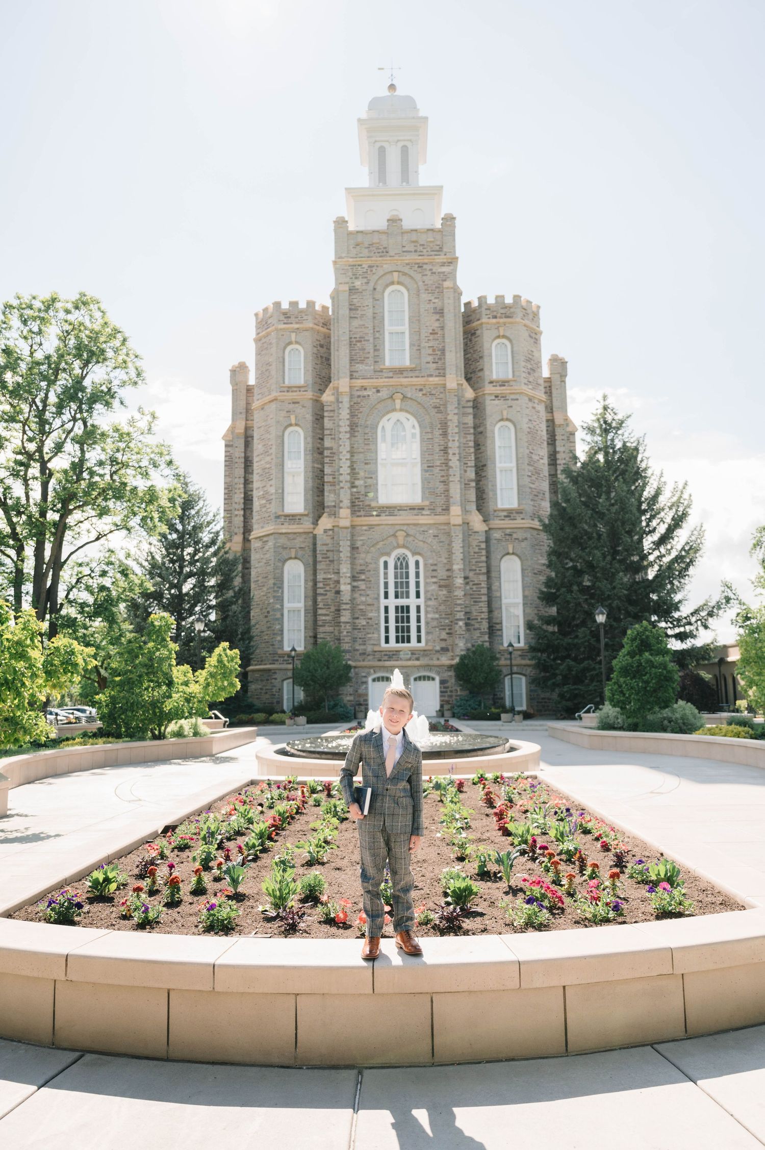 A historic stone temple with Gothic architecture stands majestically behind a circular flower garden.