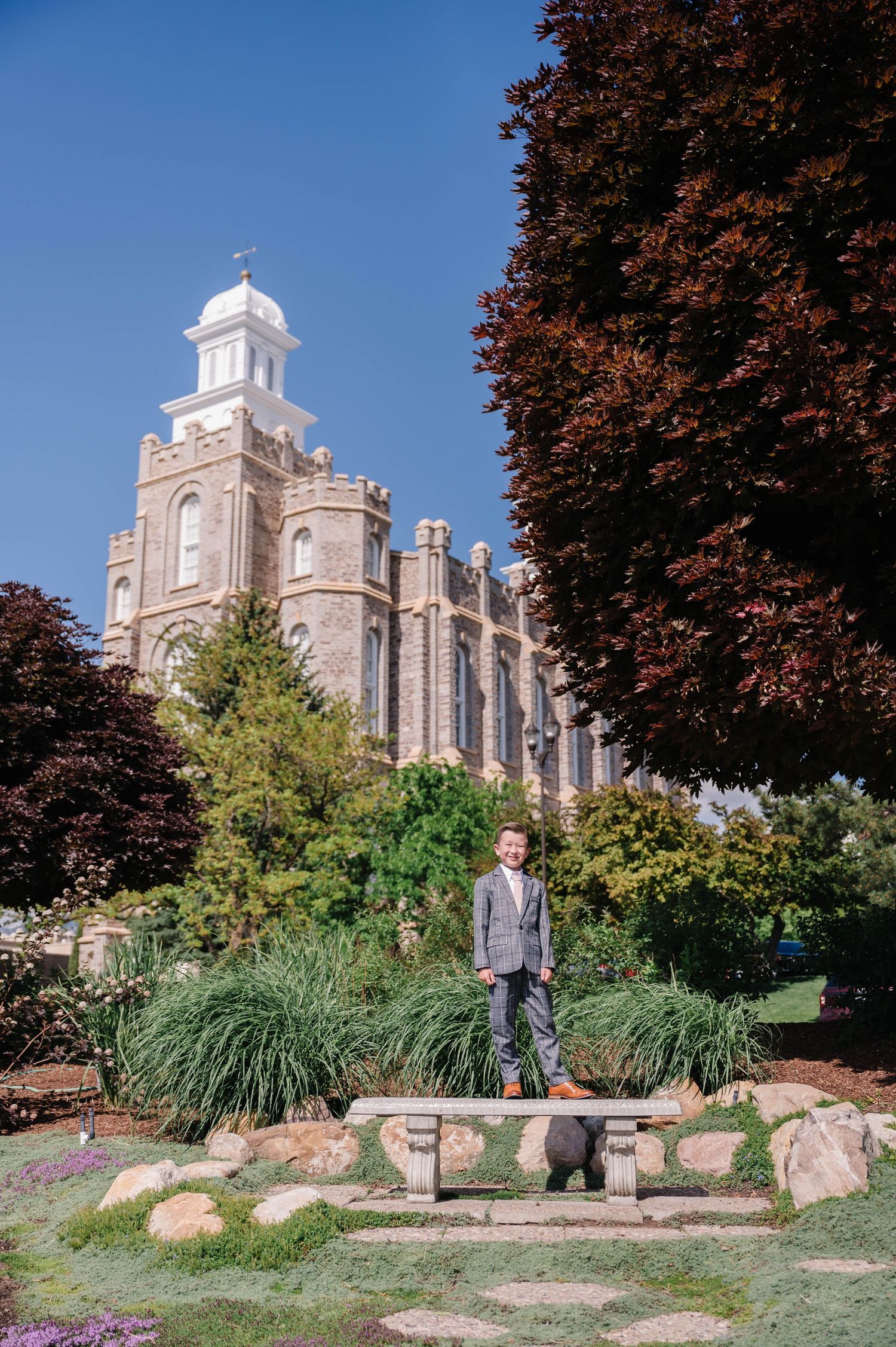 A historic stone temple with spires rises behind autumn trees and landscaping.