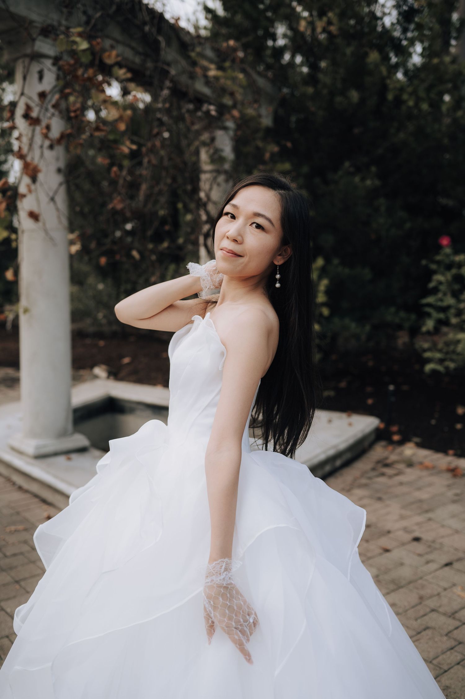 A bride in a flowing white ballgown twirls elegantly in an outdoor garden setting with classical columns.