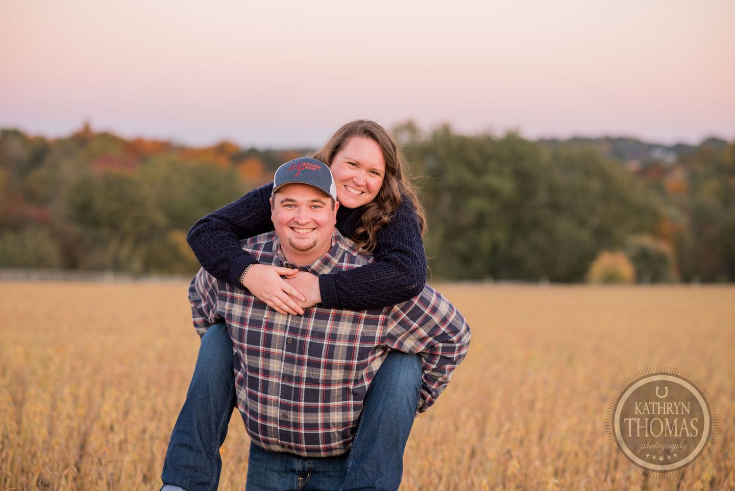 Couple enjoying a playful piggyback ride in a golden field at sunset.