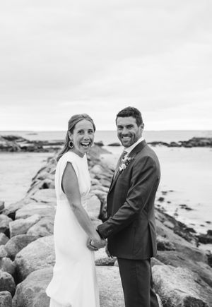 Wedding couple sharing a joyful moment on rocky coastal shoreline.