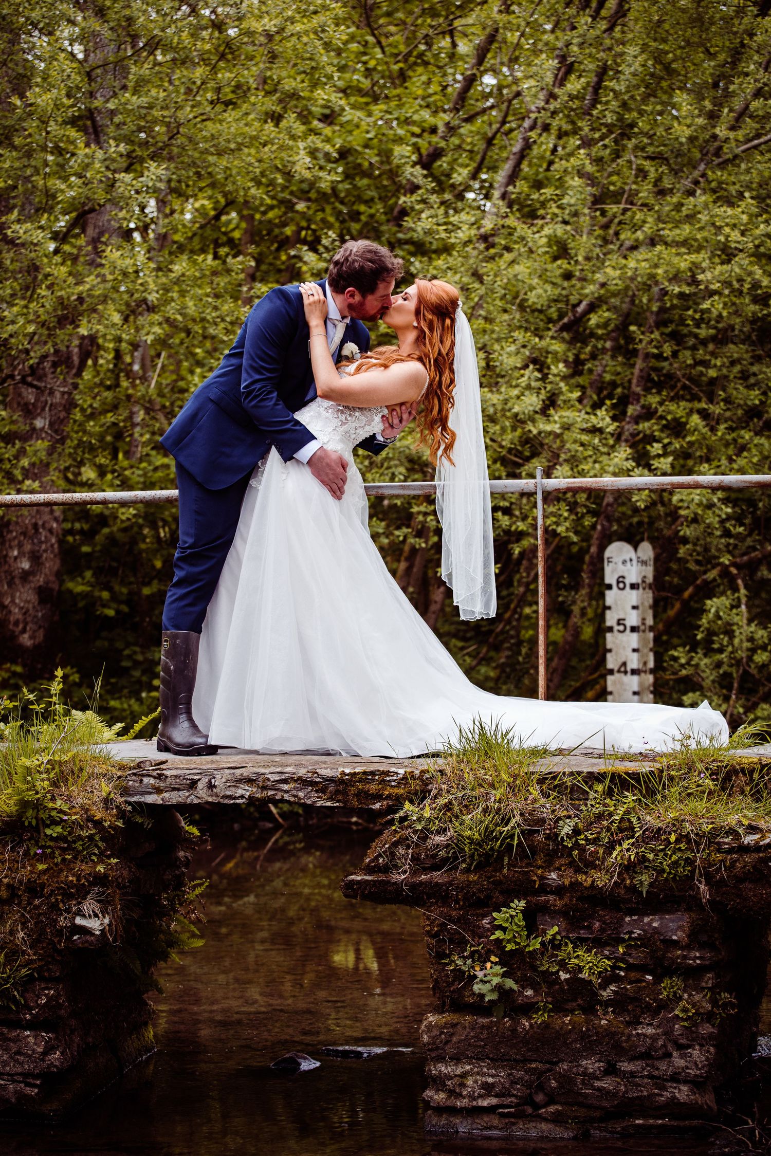 Romantic wedding photo on a rustic stone bridge over a stream.
