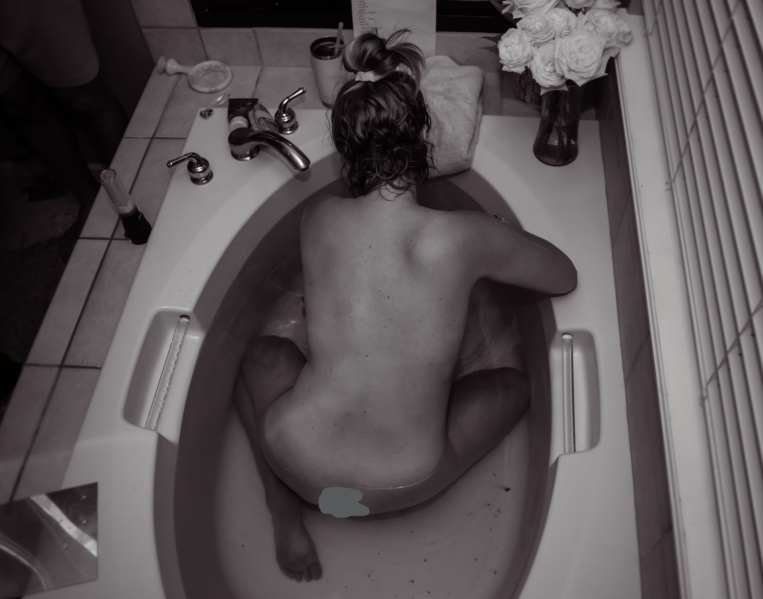 Black and white image of a pregnant woman in labor in her bathtub.