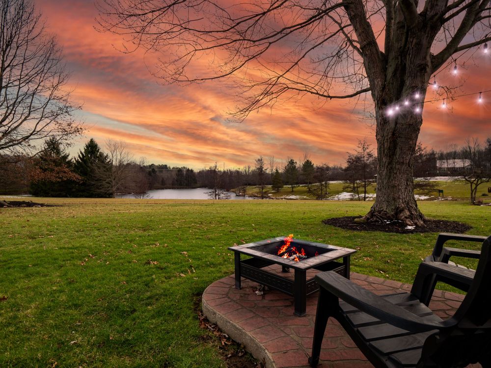Fire pit and chairs on a patio overlooking a lake during a dramatic orange sunset.
