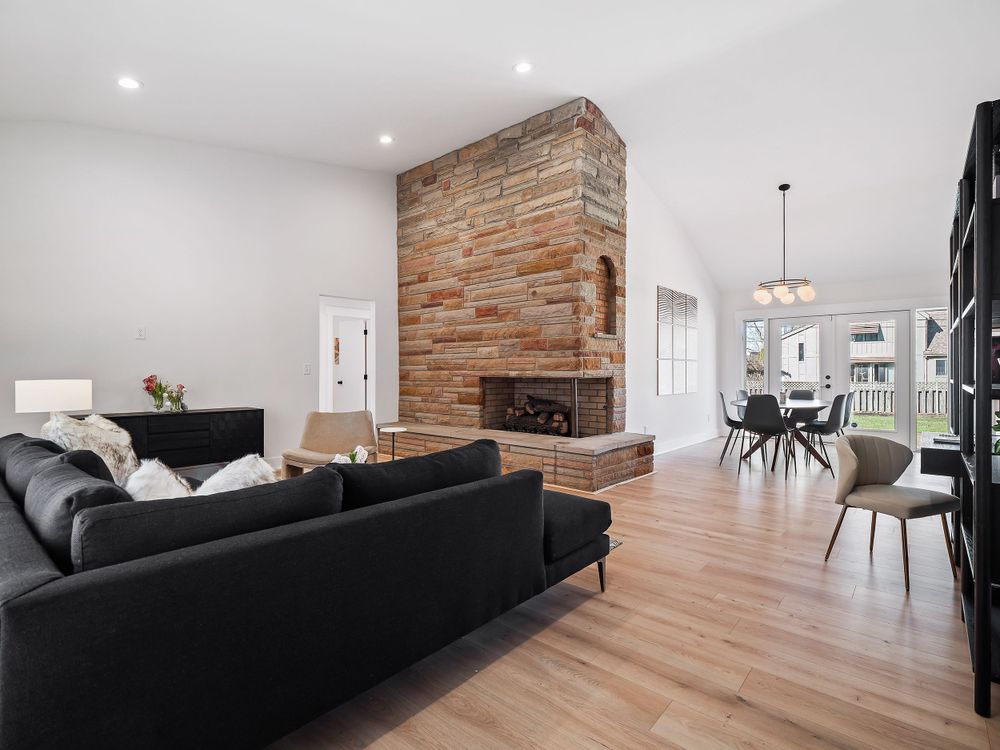 Contemporary living room featuring exposed brick fireplace wall, black sofa, and hardwood floors.