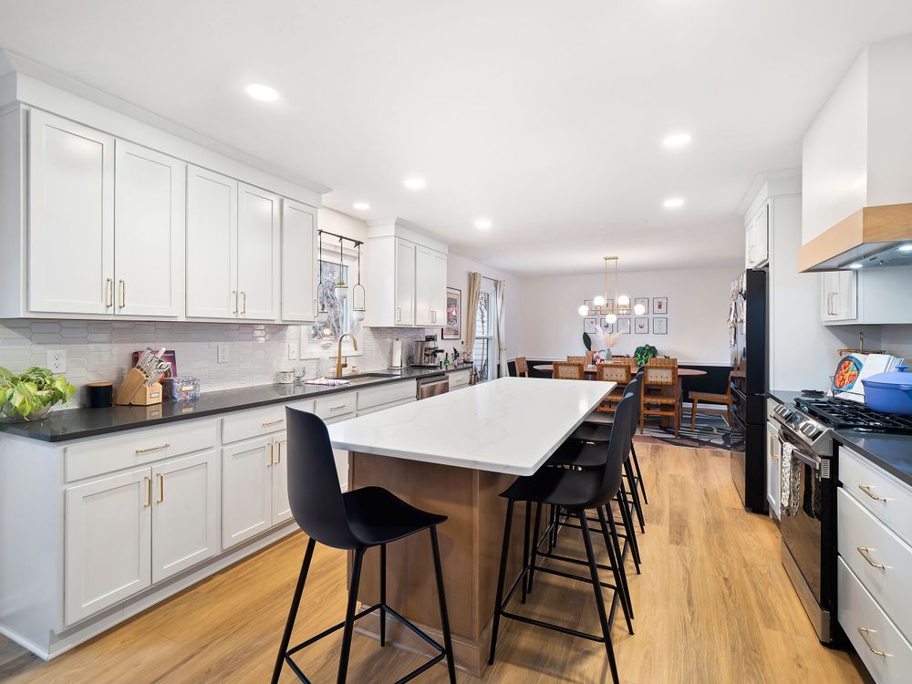 Modern white kitchen with large island, black barstools and hardwood floors.