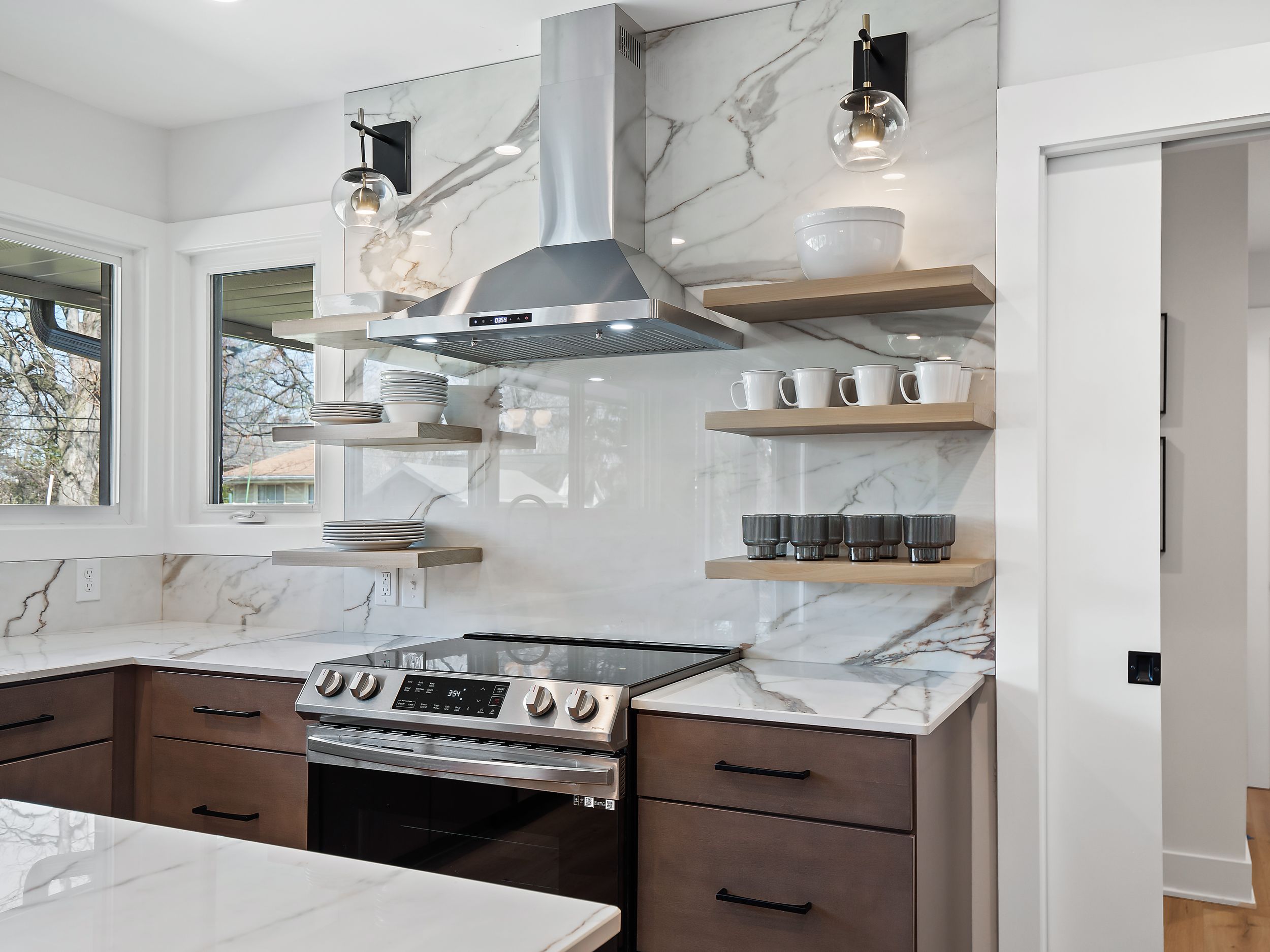 Contemporary kitchen featuring marble backsplash, floating shelves, and stainless steel appliances.