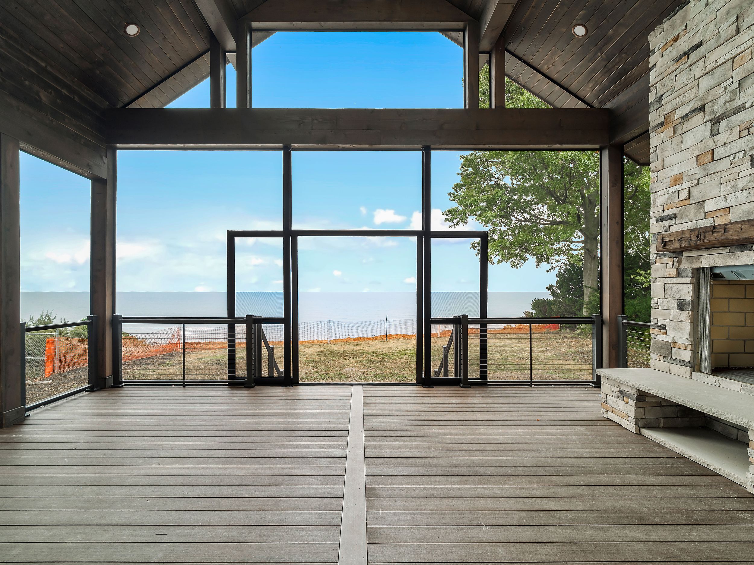 Covered deck with stone fireplace and expansive glass doors offering panoramic water views.