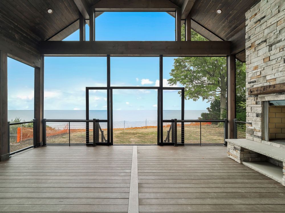 Covered deck with stone fireplace and expansive glass doors offering panoramic water views.