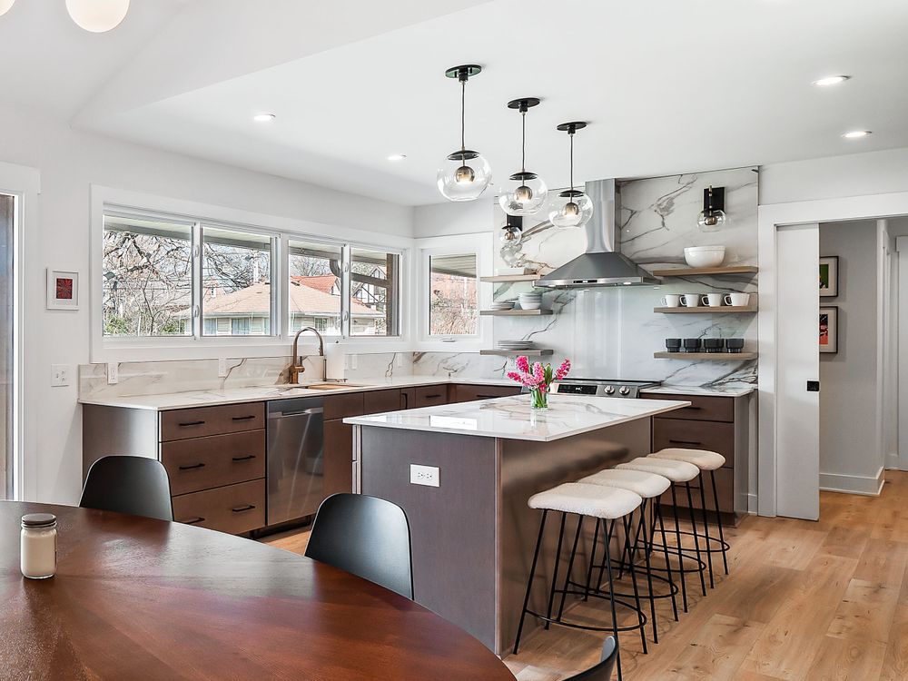 Modern white kitchen with large island, pendant lights, and dark wood cabinets.