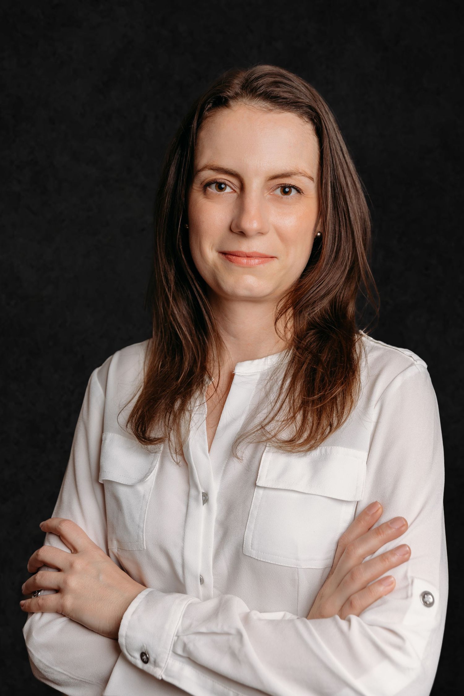 Professional portrait in white button-down shirt against dark background with crossed arms.