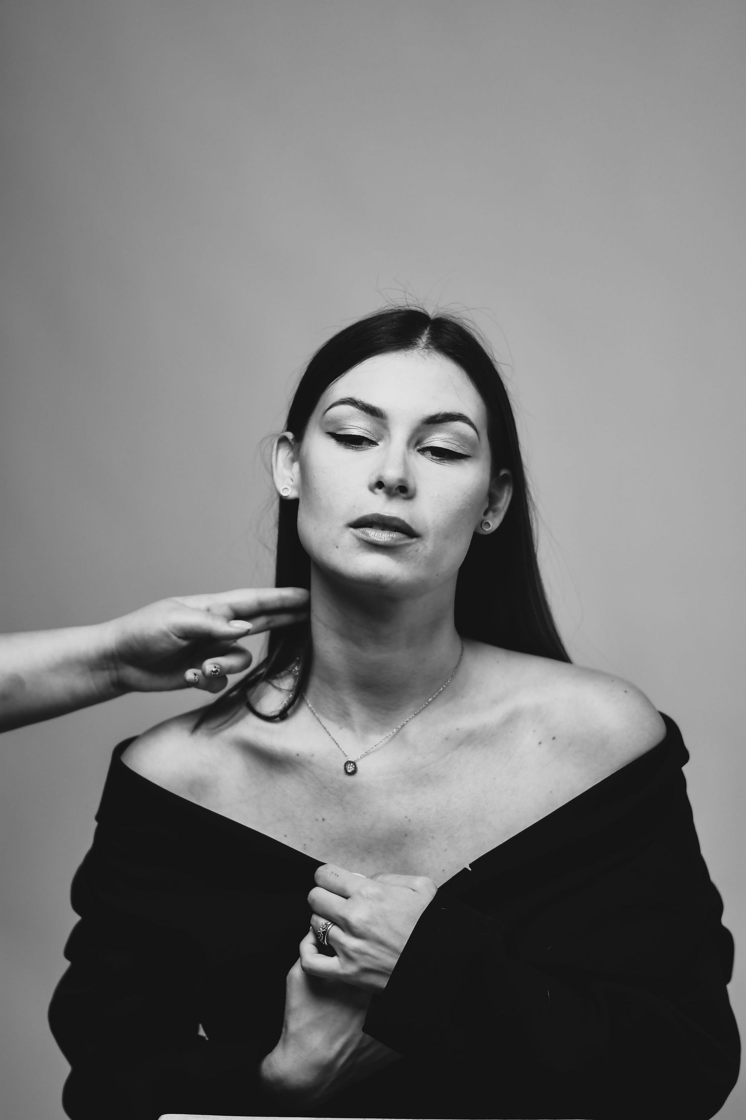 Artistic black and white portrait photo showing bare shoulders and delicate hand gesture.