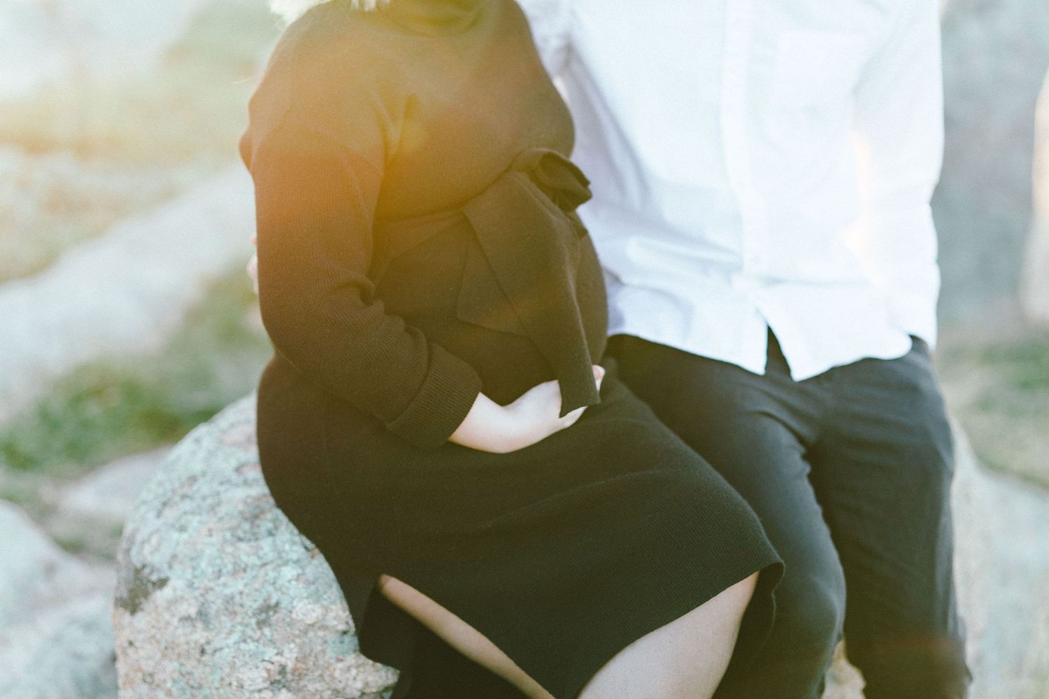 Two people share an intimate moment while sitting on rocks during sunset.