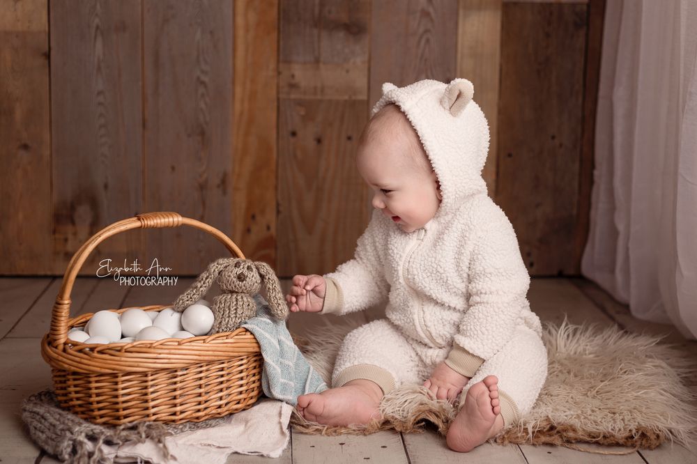 Happy baby wearing a lamb outfit and sitting next to easter egg basket with knit bunny.  Wisconsin Baby Portrait