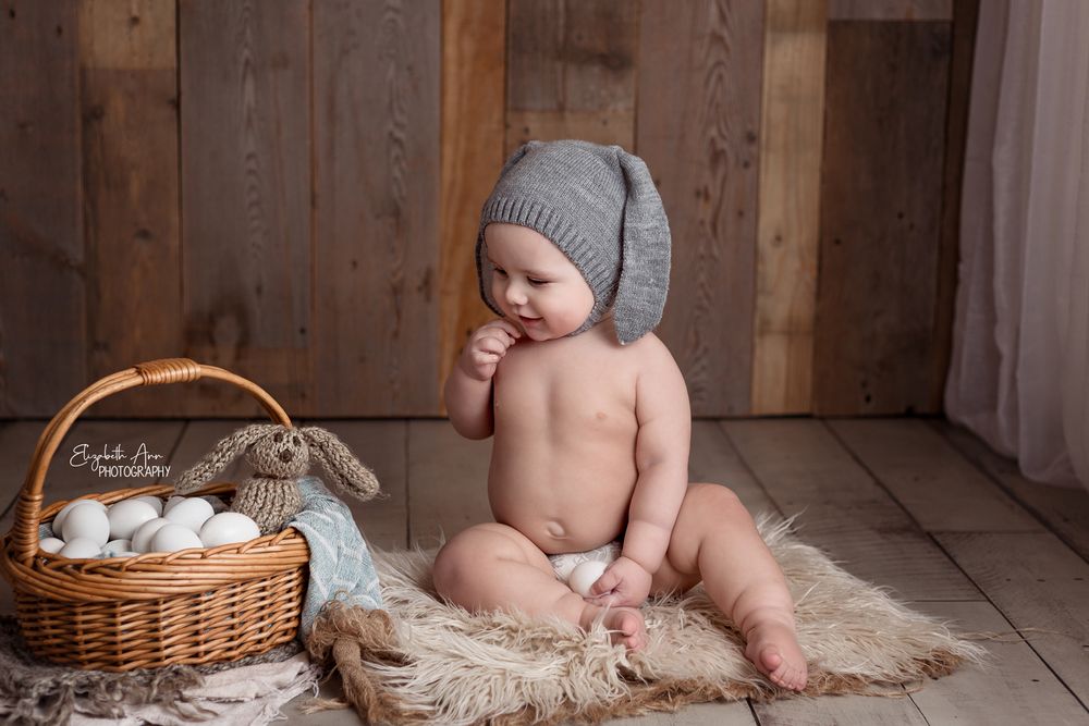 Baby sitting next to easter egg basket and wearing knit bunny hat with knit bunny.  Wisconsin Baby Portrait