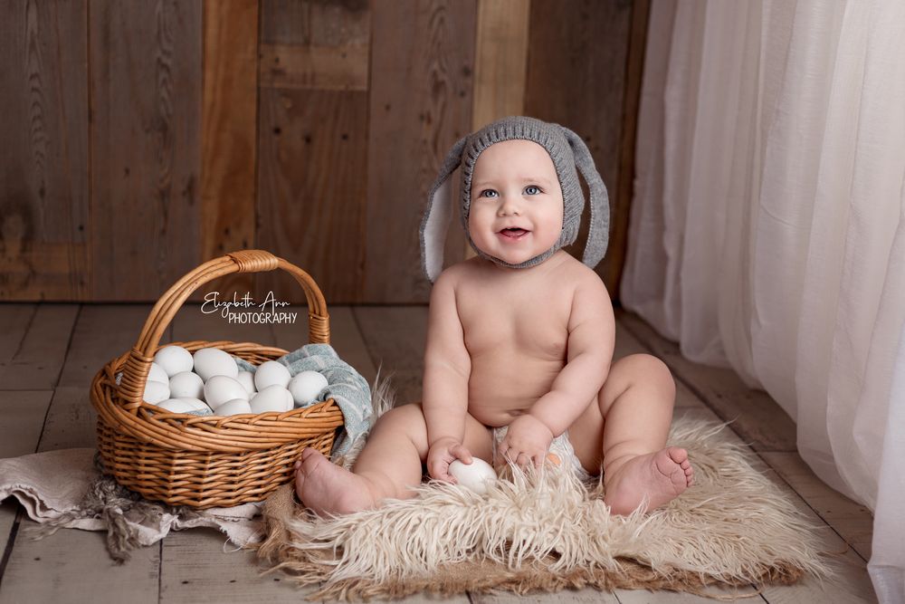 Smiling baby sitting next to easter egg basket and wearing knit bunny hat.  Wisconsin Baby Portrait