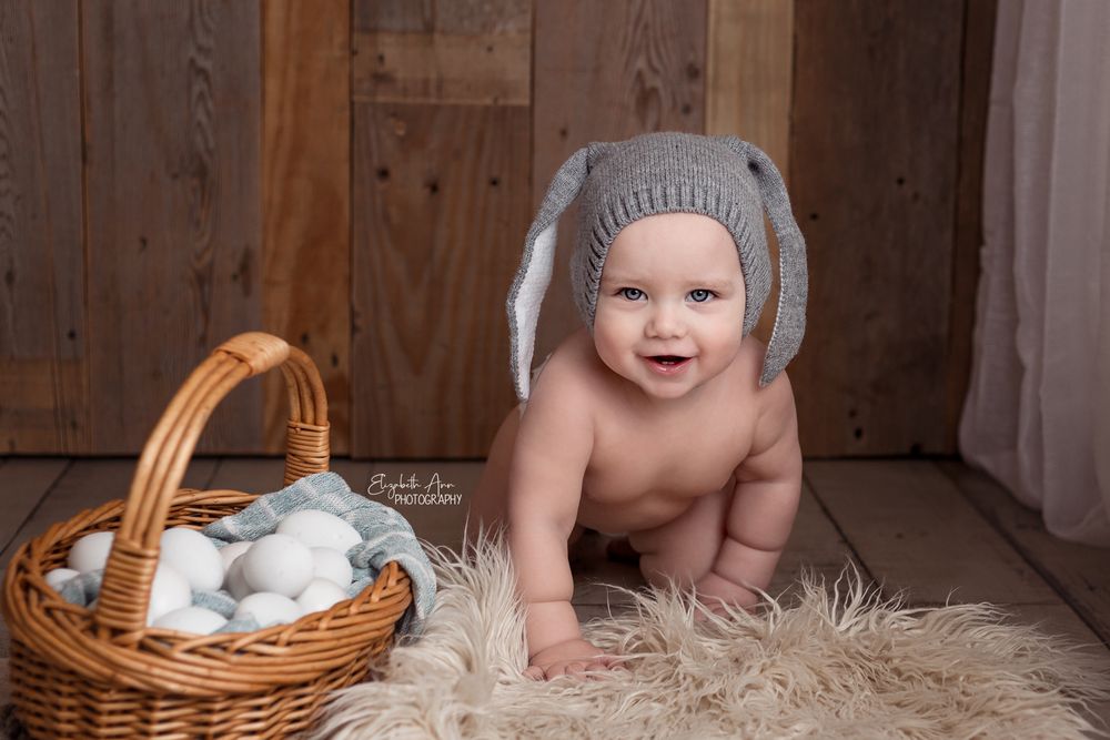 Baby crawling next to easter egg basket and wearing knit bunny hat.  Wisconsin Baby Portrait