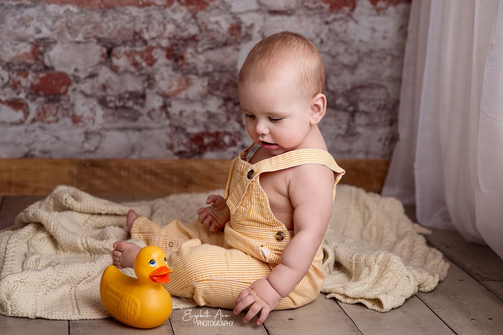 Sitting baby boy wearing vintage overalls with vintage rubber ducky, brick wall.  Wisconsin Baby Portrait
