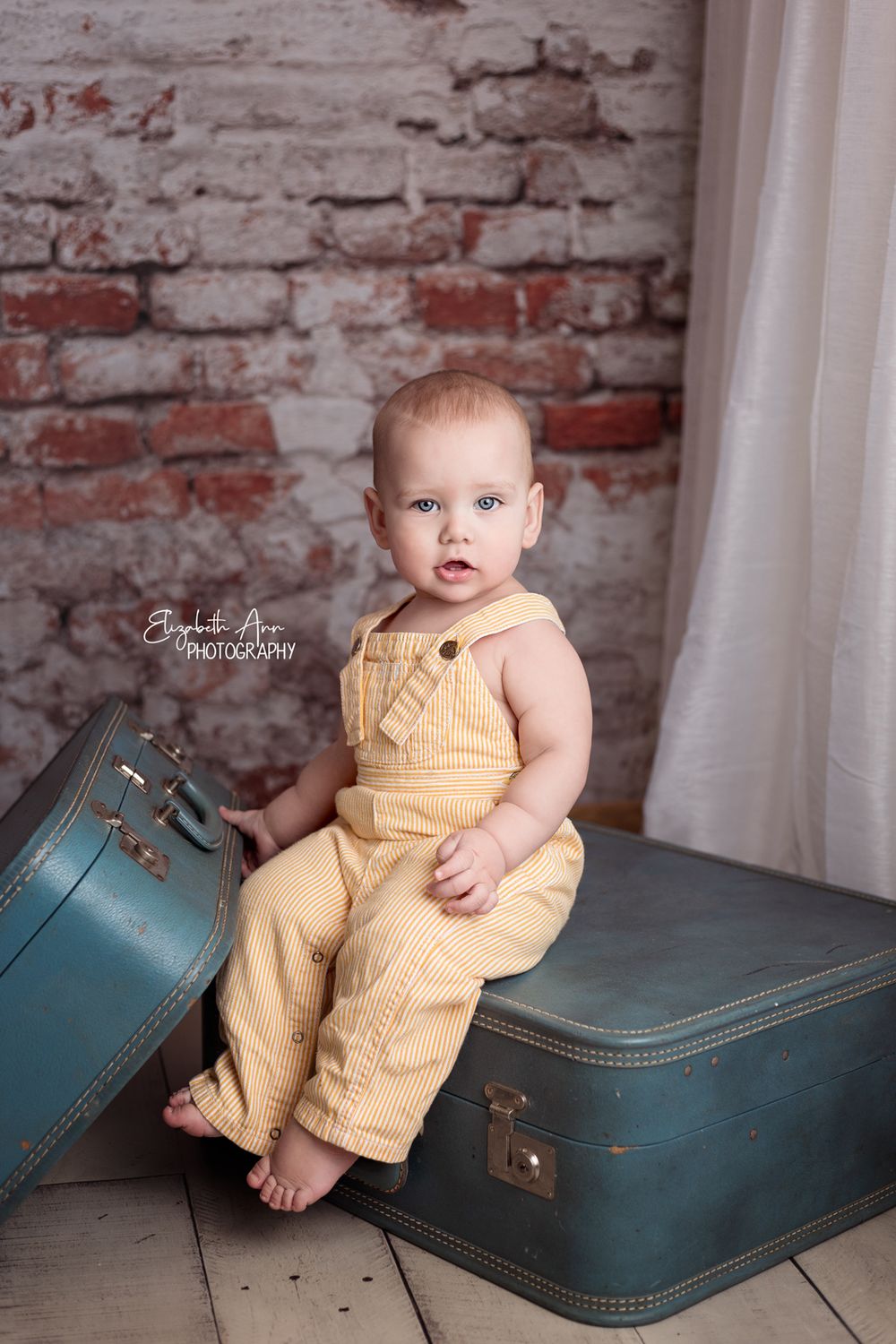 Sitting baby boy wearing vintage overalls with vintage suitcases, brick wall.  Wisconsin Baby Portrait