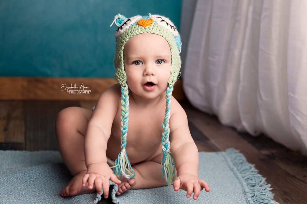 Baby sitting with an owl hat and blue wall. Wisconsin Baby Studio Portrait