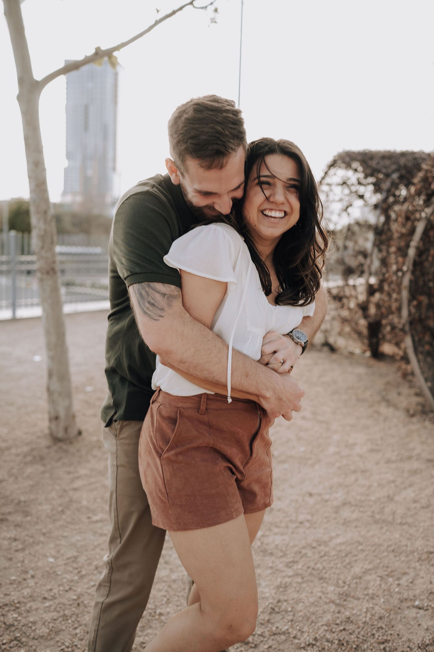 A tender embrace captured between a couple outdoors with natural lighting and trees in the background.