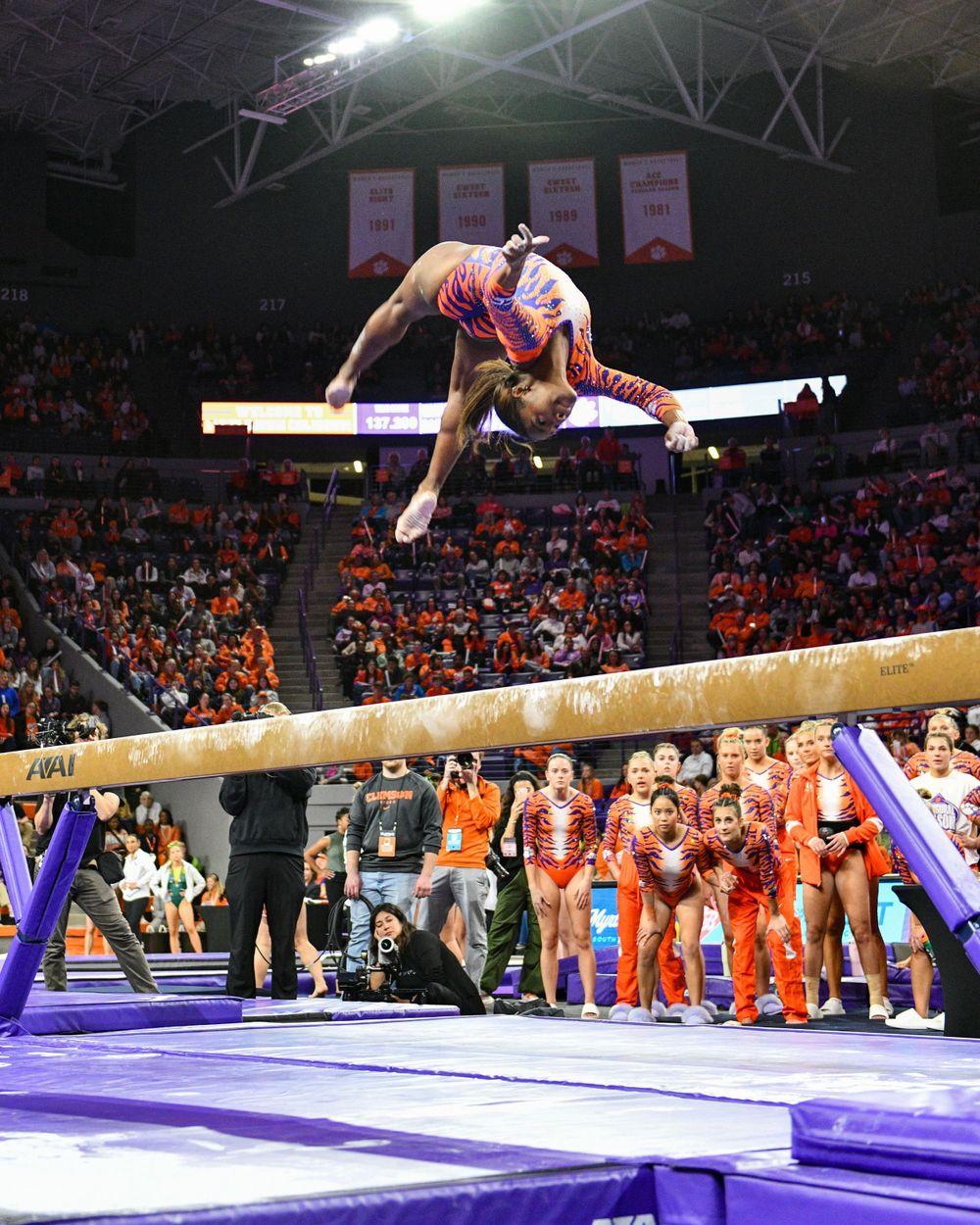 Gymnast performs an impressive balance beam routine in a packed indoor arena.