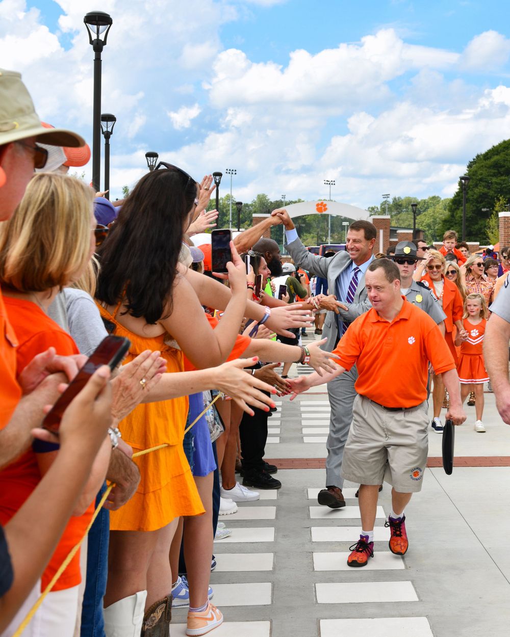 Fans line up along a walkway to greet and high-five someone in orange Clemson attire.