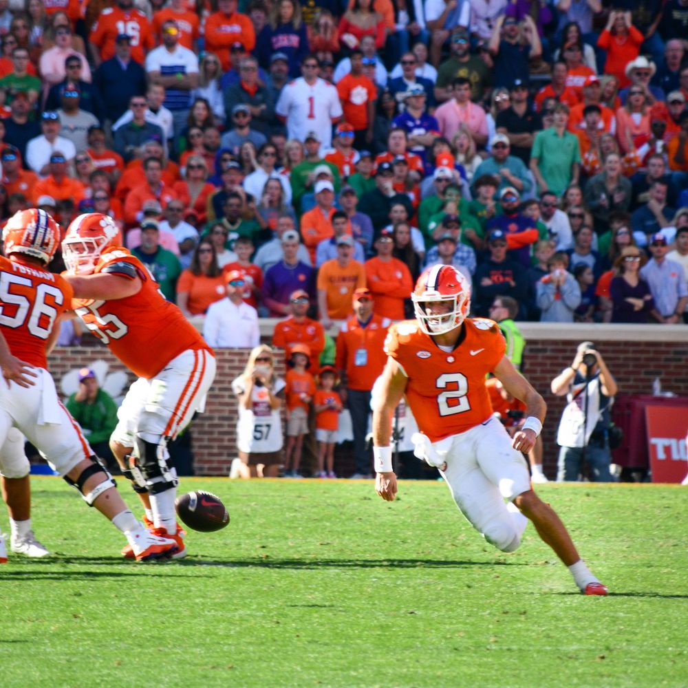 Football player in orange jersey running with the ball during a game at Memorial Stadium.
