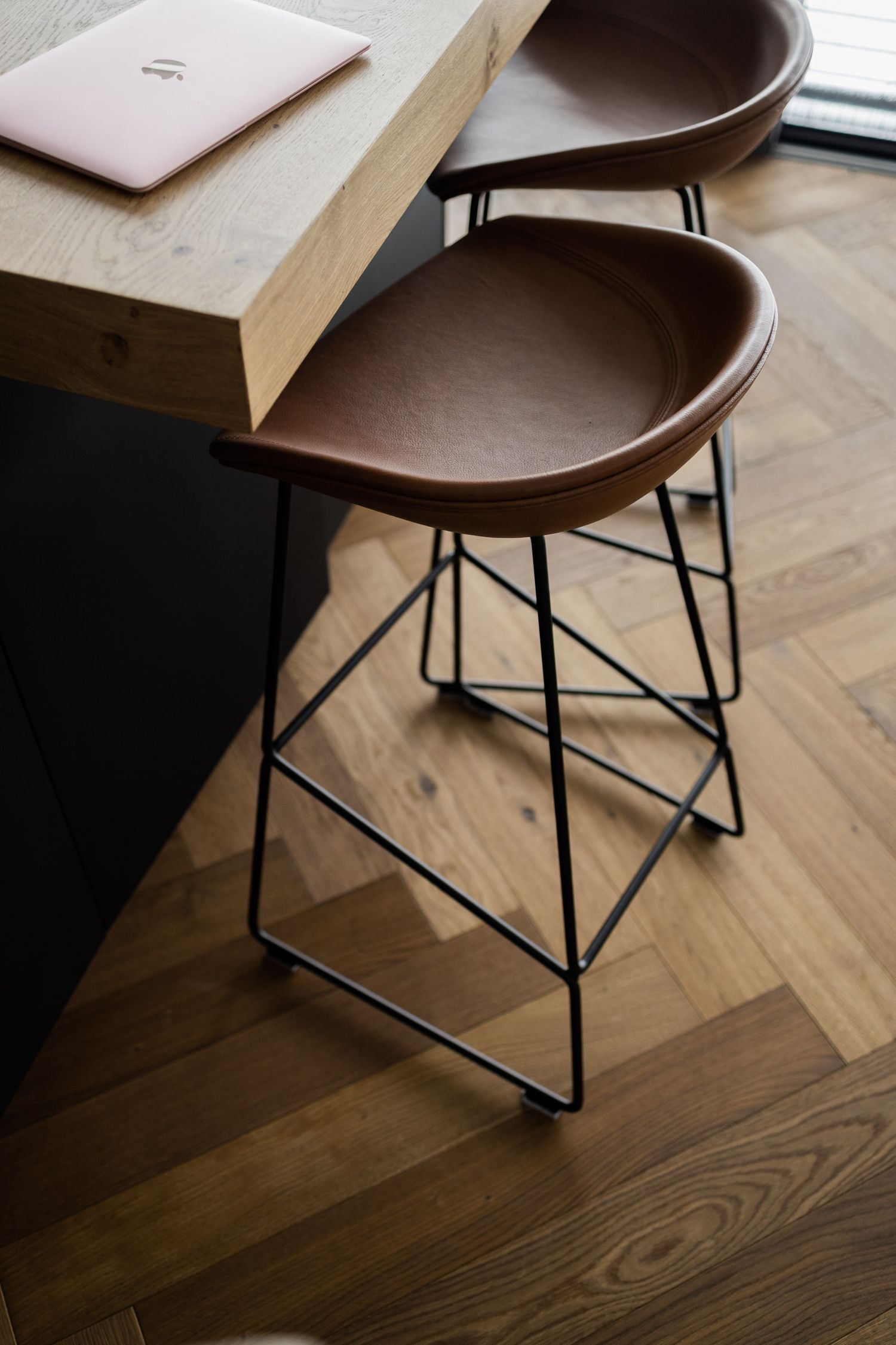 Modern brown chair with metal legs on herringbone wooden floor in minimalist setting.