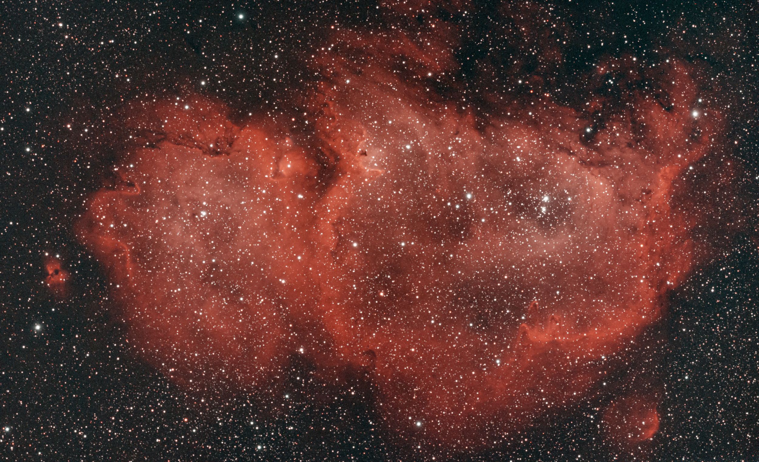 A deep space image shows the Heart Nebula's glowing red hydrogen gas clouds spanning light-years across.