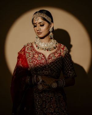 South Asian bride in red and gold embellished dress with traditional jewelry and makeup.