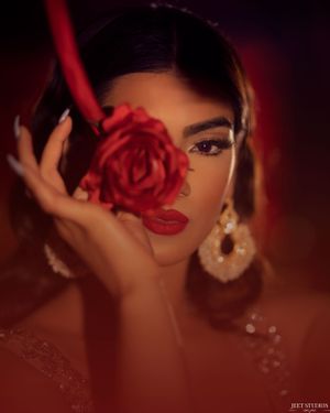 A dramatic portrait featuring a red rose held against a face with glamorous makeup in moody lighting.