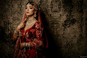 Dramatic bridal portrait in red traditional attire against textured vintage wallpaper.