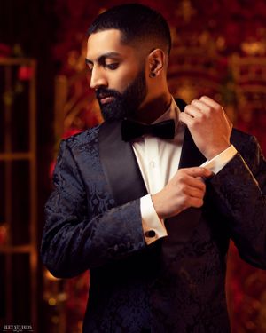 Groom adjusting cufflink wearing navy jacquard tuxedo with bowtie.