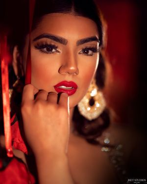 Glamorous beauty portrait with red lipstick and dangling earrings against a dark background.