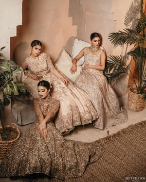 Three models in embellished cream lehengas posed artistically in a modern interior setting.