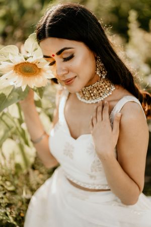 A bride in white holding a sunflower poses with closed eyes in golden sunlight.