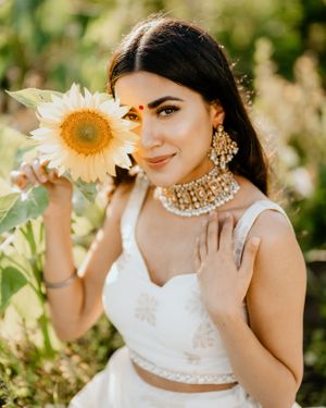 A bride in traditional Indian attire poses with a sunflower in a sunny garden setting.