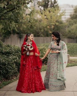 Two women in traditional Indian attire walk together wearing red and mint green lehengas.