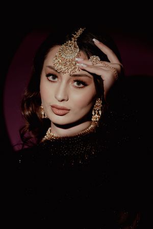 Dramatic portrait with ornate gold jewelry and makeup against dark background.