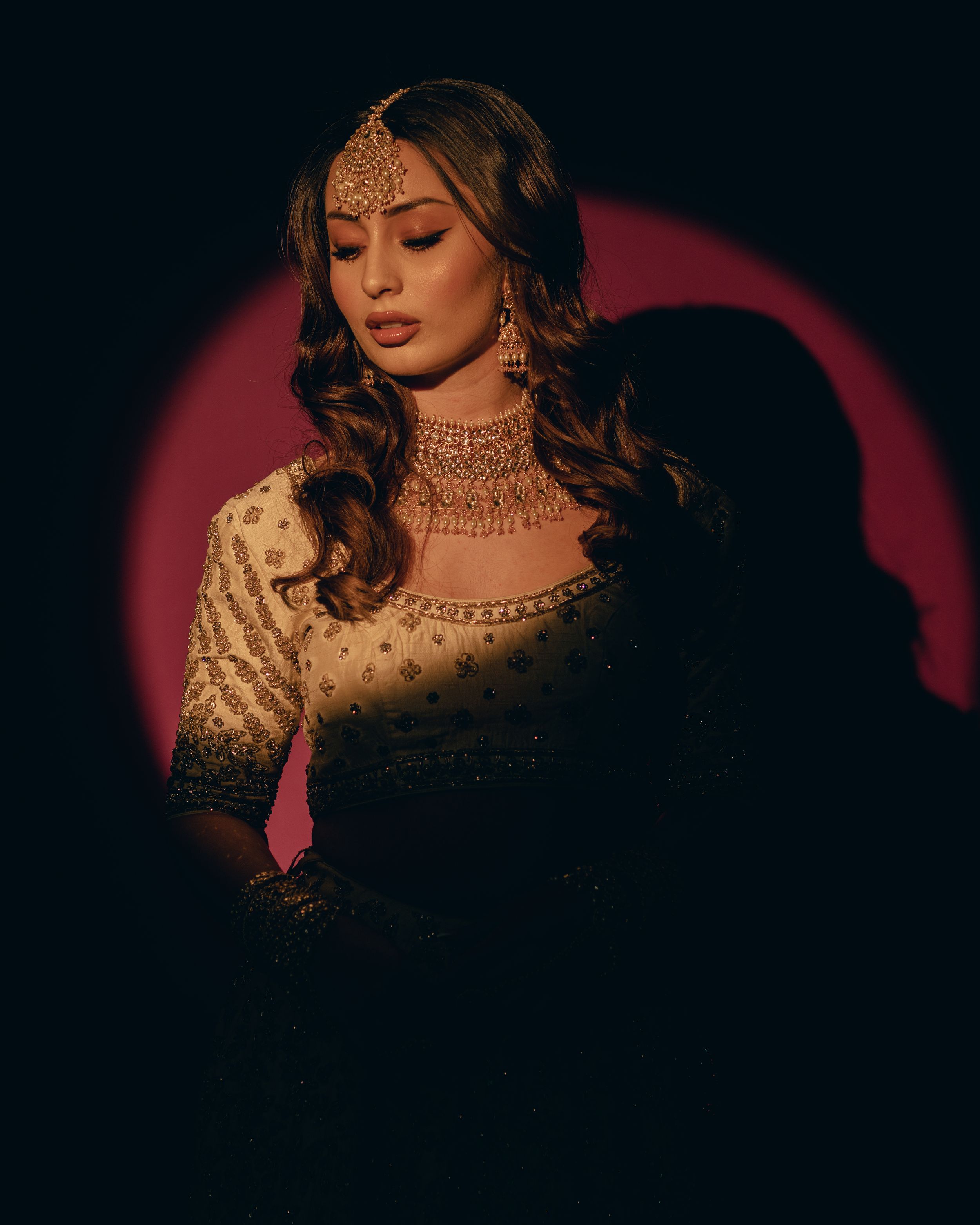 Moody portrait in golden traditional Indian bridal attire against dark backdrop.