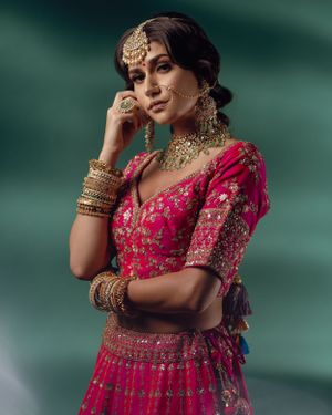 Woman in pink embroidered lehenga with traditional Indian bridal jewelry and accessories poses elegantly.