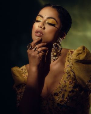 Artistic portrait showcasing intricate gold jewelry and yellow embroidered outfit with dramatic makeup.