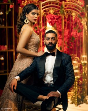 Couple in formal attire posing against ornate red and gold backdrop.