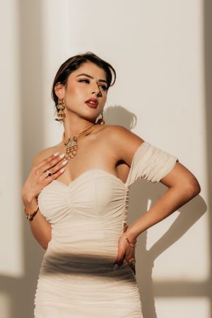 Elegant portrait featuring cream formal dress and gold statement jewelry in natural lighting.