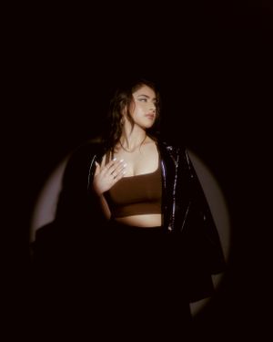 Dramatic low-key portrait showing silhouette wearing leather jacket and crop top in spotlight.