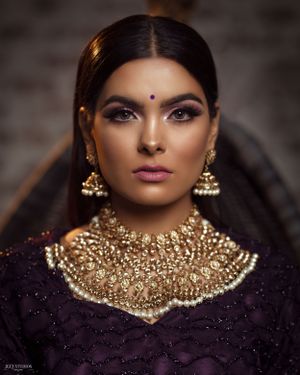 Traditional South Asian bridal portrait showcasing ornate gold jewelry and purple attire.