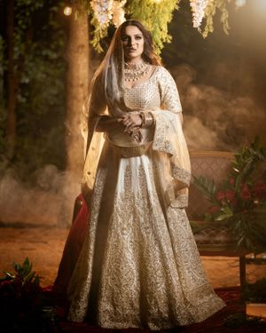Ethereal bridal portrait in a white lehenga under dreamy outdoor lighting with hanging florals.