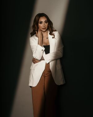 Professional fashion portrait featuring white blazer and brown pants in dramatic studio lighting.